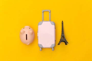 Traveled to Paris. Mini plastic travel suitcase and statuette of the Eiffel Tower, piggy bank on yellow background. Top view. Flat lay