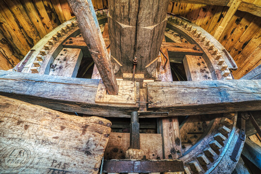 A wooden cog with a shaft used for driving a grindstone in a rural windmill for wheat grinding. Industrial interior with a toothed gear moved by wind mill blades drives a powerful milling machine