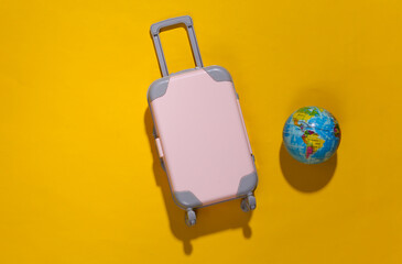 Travel minimalism. Mini plastic travel suitcase and globe on yellow background with deep shadow. Minimal style. Top view, flat lay