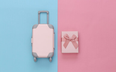 Travel concept. Mini plastic travel suitcase and gift boxes on pink blue pastel background. Minimal style. Top view, flat lay