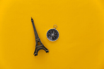 Minimalism travel, adventure flat lay. Compass and eiffel tower figurine on a yellow background. Top view