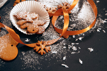 Christmas freshly baked gingerbread cookies sprinkled with powdered sugar with snowflakes and ribbon on black background. Holiday food, homemade baking, Christmas and New Year traditions. - 383779549