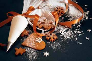 Christmas gingerbread cookies with confectionery mastic snowflakes and pastry bag with icing on black background. Holiday food, homemade baking, Christmas and New Year traditions. - 383779748