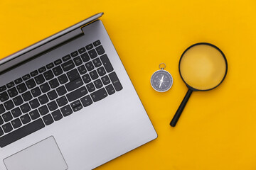 Laptop and compass, magnifier on yellow background. Online business or travel. Top view