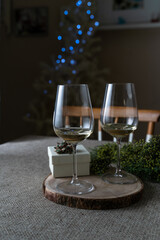 Party gift box and glasses of white wine with defocused Christmas tree lights. Christmas at home