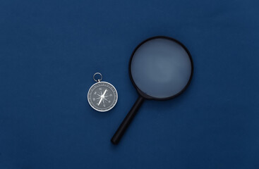 Minimalism travel, adventure flat lay. Compass and magnifier on classic blue background. Top view