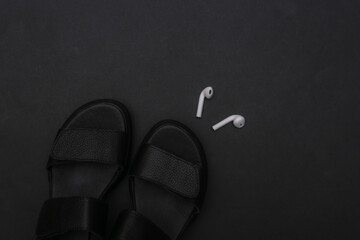Leather sandals and wireless headphones on a black background. Top view