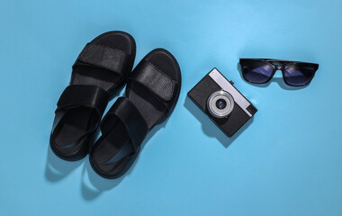 Travel planning. Flat lay composition of women's sandals, camera and sunglasses on a bright blue background. Top view