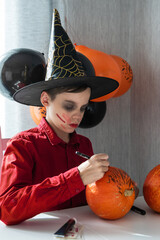 Happy teen boy in costume preparing for the Halloween celebration drawing a pumpkin. Halloween...