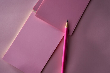 Pink memo note pad and pink colored pencil on pink background.