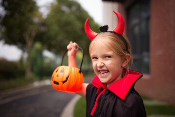 Little Girl in costume of devil with red horns in park. Happy Halloween concept
