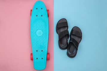 Flat lay composition of mini cruiser board and sandals on pink blue background. Top view