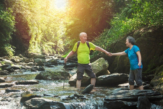 Senior couple walking across small river in nature park