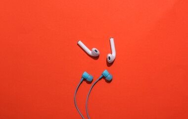 Wireless earbuds and classic wired earbuds on bright orange background. Top view