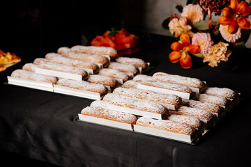 Vanilla eclairs sprinkled with powdered sugar and flowers bouquet