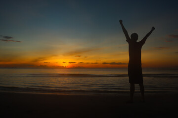Fototapeta na wymiar Silhouette man raise their arms on the beach in morning with sun rise.