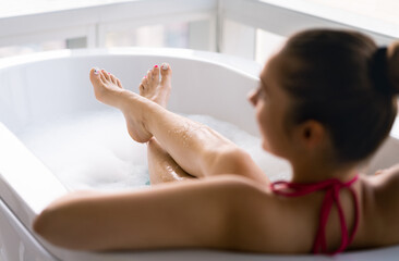 Obraz na płótnie Canvas Woman in bubble bath after pedicure and toe nail polish. Lady relaxing in bathtub. Clean wet legs and feet in tub with foam. Pamper and therapy treatment in spa. Girl enjoying hot water in the morning