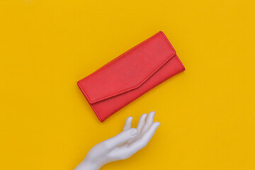 The mannequin's white hand touches leather wallet on yellow background. Top view