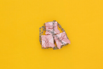 Gift boxes wrapped in a steel chain on a yellow background. Top view