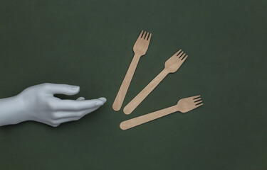 Wooden eco forks and mannequin hand on green background