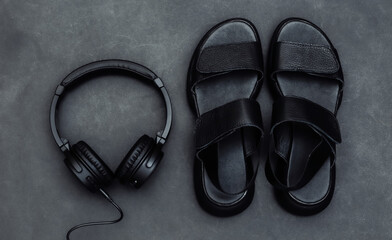 Black leather sandals and stereo headphones on a black background. Top view
