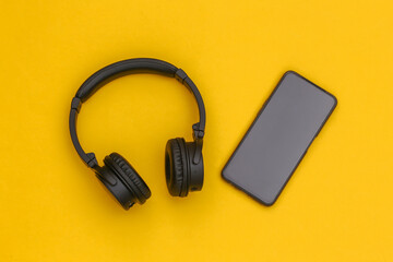 Wireless stereo headphones and smartphone on yellow background. Top view