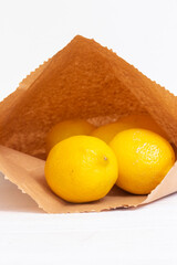 Lemons in a brown paper bag on a white wood background.  Environmentally friendly packaging concept