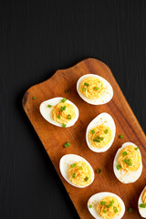 Homemade Deviled Eggs with Chives on a rustic wooden board on a black background, top view. Flat lay, overhead, from above. Space for text.