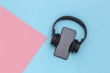 Smartphone with wireless stereo headphones on pink blue pastel background. Top view