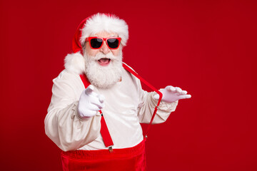 Fototapeta na wymiar Close-up portrait of his he nice handsome cheerful cheery excited bearded fat Santa pulling suspenders pointing at you having fun invite date isolated bright vivid shine vibrant red color background