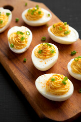 Homemade Deviled Eggs with Chives on a rustic wooden board on a black background, side view. Close-up.