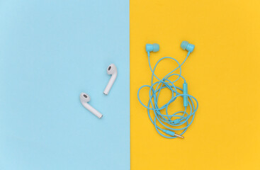 Wireless earphones and wired tangled headphones on yellow background. Top view. Flat lay