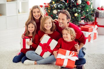 Obraz na płótnie Canvas Portrait of nice attractive cheerful big full family small little kids sitting on carpet holding in hands giftboxes December holly jolly day in light white interior apartment house indoor