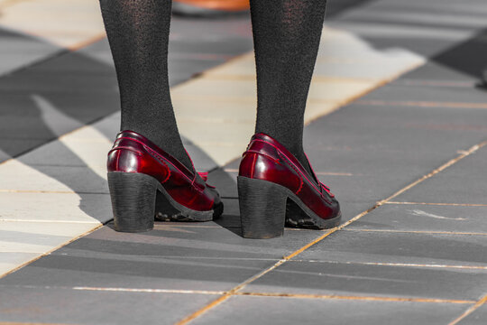 Halloween themes, dressing up for party. Closeup shot of new shiny red shoes with heel. Young woman standing on the street, black stockings, natural sunset light, warm october afternoon.
