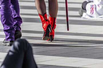 Halloween period, closeup of bright red shiny shoes. Female style, fantasy outfit, cosplayer, girls dressing up for the event. Low angle view, footwear, feet, street atmosphere, natural daylight.