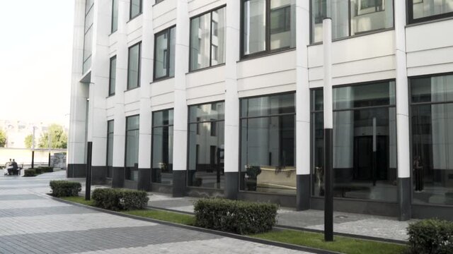 Details of a modern, stylish and innovative office building in black and white colors. Action. Business center with big glass windowc and small green bushes growing along its perimeter.