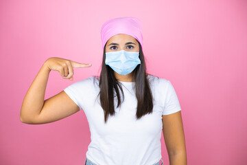 Young beautiful woman wearing pink headscarf over isolated pink background pointing the mask. Warning expression with negative and serious gesture on the face.