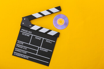 Film clapper board and cd on yellow background. Cinema industry, entertainment. Top view
