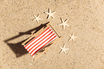 Summer beach travel vacation concept. Mini beach deck chair on sand with starfish at bright sunny day.