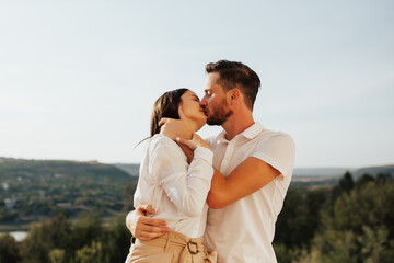 Close up portrait of romantic couple in love in white shirts are kissing with the green mountain landscape in the background.