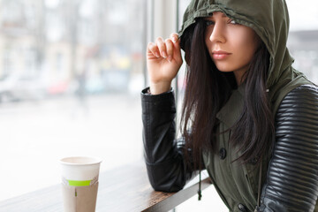 girl in hood is drinking coffee in street cafe