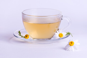 Cup of hot herbal tea with chamomile flowers against a light background.