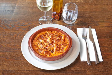 Silverware on Brown wooden table and White plate gratin of macaroni in ceramic bowl.