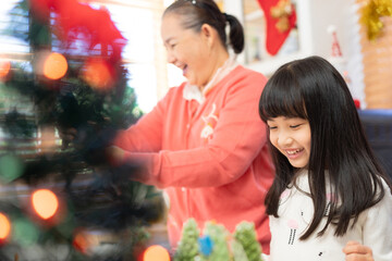 Fototapeta na wymiar Long hair with bangs Asian lovely girl smile happily looking at Christmas tree shaped cupcakes, feel proud to be making cupcakes together with grandparents for Christmas.