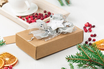 Christmas decoration, cup of coffee, homemade sweet present in festive box, empty tag, pine cones and branches on white wooden background.
