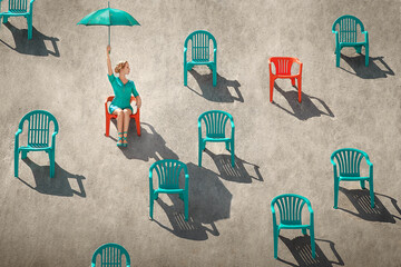 Young blonde woman holding up a turquoise umbrella on a beach, sitting through many red and teal...