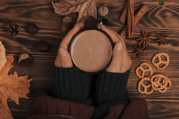 Top view composition with young woman's hands in red blue sweater, vintage styled cup of hot...