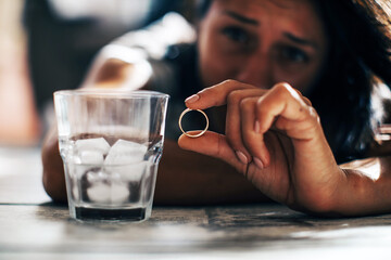 Doubtful young woman holding wedding ring in hand, feeling unsure hesitating about engagement proposal, sad wife thinking about breaking up or getting divorced concept, unhappy marriage

