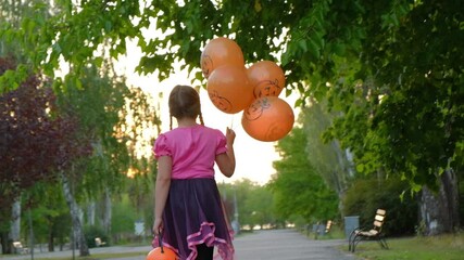 Halloween kids. child with pumpkin candy bucket walks along the alley. Girl in witch costume playing with orange balloon in autumn park. A Child in a carnival costume outdoors - Powered by Adobe