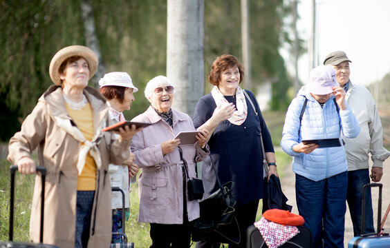 A group of positive senior elderly people travelers using tablets waiting for train before going on a trip..